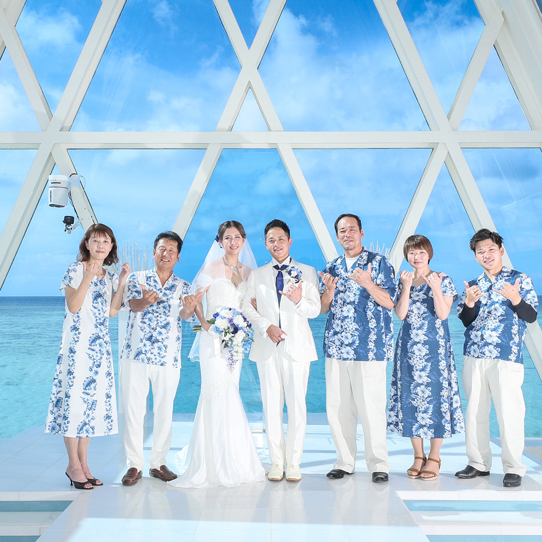 沖縄のチャペルでアロハシャツとムームーを着た家族と新郎新婦が記念撮影|青い海と空に映えるリンクコーデ